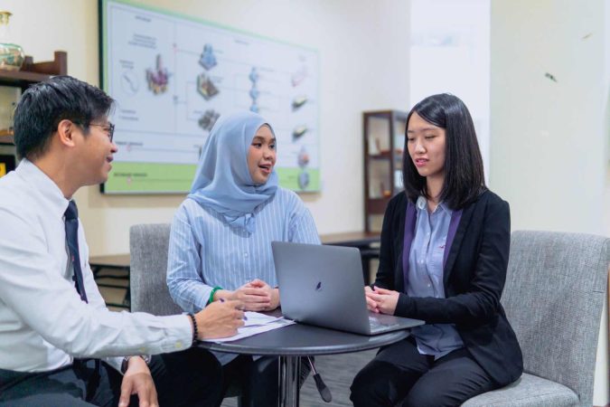 A diverse team of professionals from the Brunei Energy Services & Trading Company engaging in a collaborative discussion around a laptop in a modern office setting.