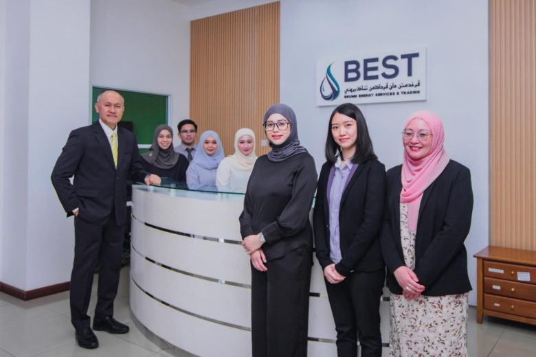 A diverse team of professionals posing with a sense of pride in their office reception area, featuring the company's logo "Brunei Energy Services & Trading Company" in the background.